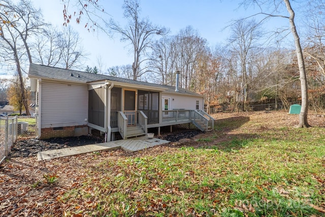 back of property with a sunroom, a deck, and a lawn