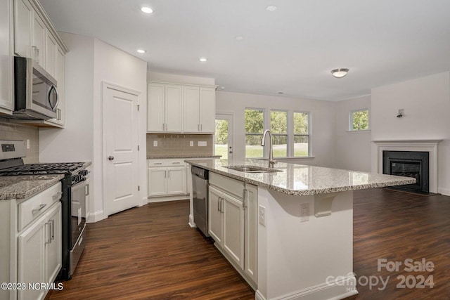 kitchen with appliances with stainless steel finishes, dark hardwood / wood-style flooring, a kitchen island with sink, sink, and white cabinets