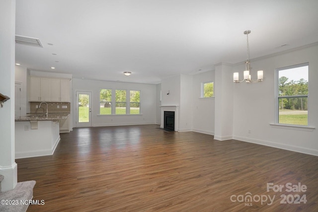 unfurnished living room featuring dark hardwood / wood-style floors, ornamental molding, and an inviting chandelier