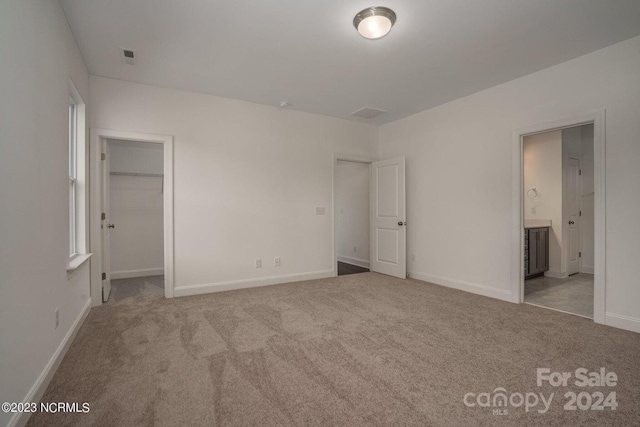 unfurnished bedroom with ensuite bath, a closet, and light colored carpet