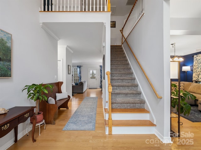 stairs featuring crown molding, wood-type flooring, and a notable chandelier