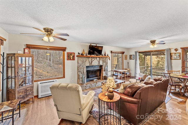 living room with light hardwood / wood-style floors, a stone fireplace, a textured ceiling, and heating unit