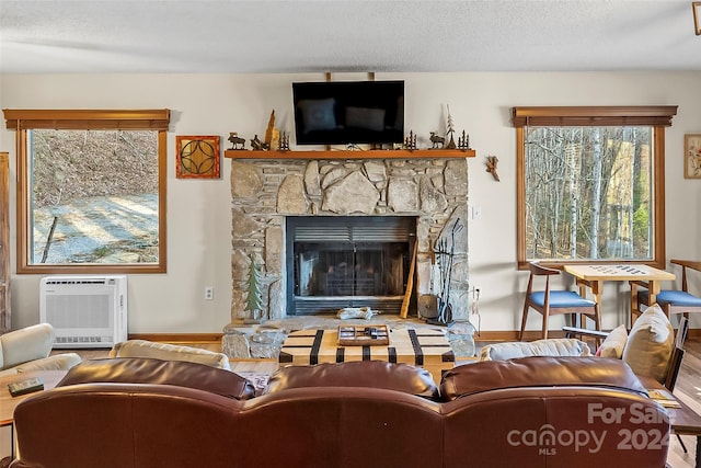 living room featuring a wall mounted air conditioner, a textured ceiling, heating unit, hardwood / wood-style floors, and a stone fireplace