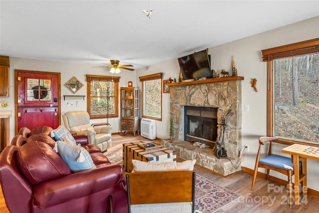 living room with ceiling fan, light hardwood / wood-style floors, and a stone fireplace