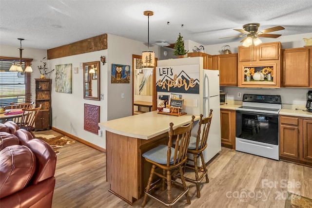 kitchen with a textured ceiling, decorative light fixtures, white appliances, and light wood-type flooring