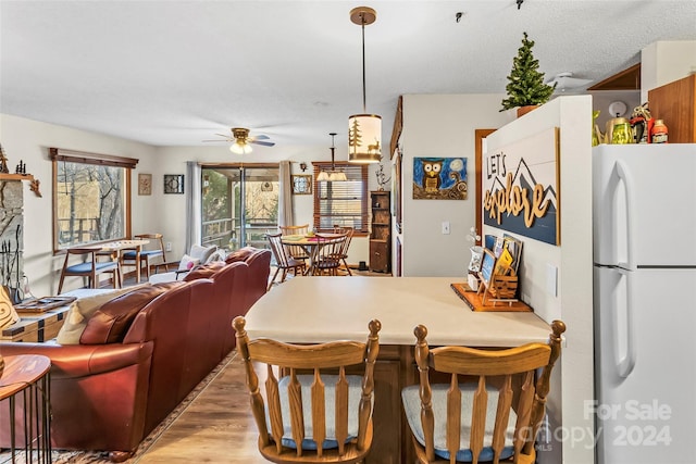 dining area featuring a fireplace, a textured ceiling, light hardwood / wood-style floors, and ceiling fan