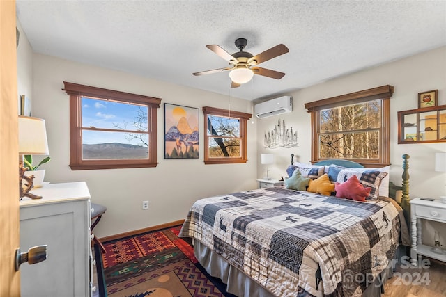 bedroom with a textured ceiling, ceiling fan, wood-type flooring, and a wall mounted air conditioner