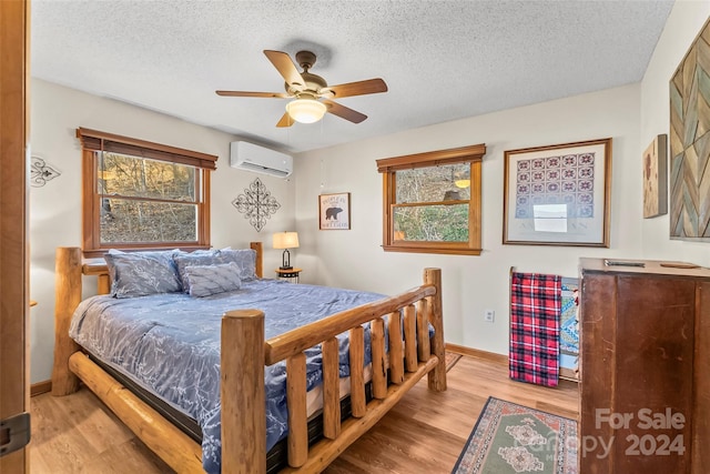 bedroom with a textured ceiling, ceiling fan, light hardwood / wood-style flooring, and a wall mounted air conditioner