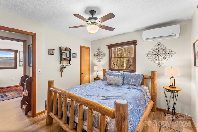 bedroom featuring a textured ceiling, ceiling fan, light hardwood / wood-style flooring, and a wall mounted air conditioner