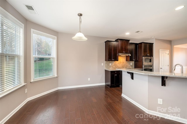 kitchen featuring pendant lighting, a kitchen breakfast bar, dark hardwood / wood-style floors, appliances with stainless steel finishes, and light stone counters