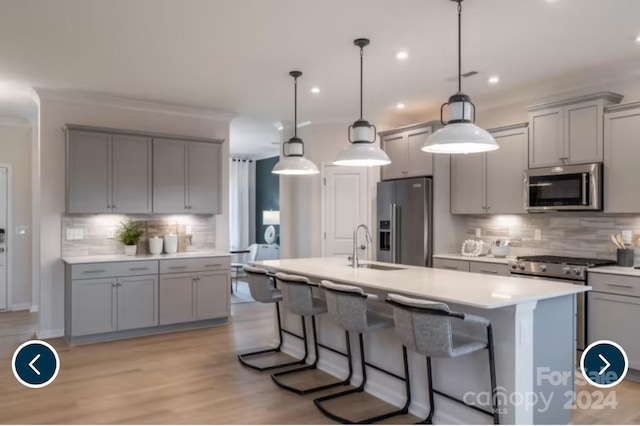 kitchen with hanging light fixtures, appliances with stainless steel finishes, tasteful backsplash, and a kitchen island with sink