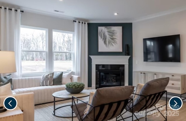 living room with recessed lighting, wood finished floors, visible vents, ornamental molding, and a glass covered fireplace