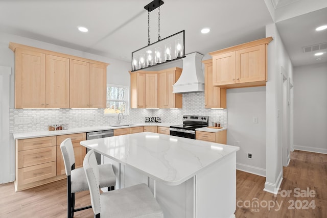 kitchen featuring sink, light hardwood / wood-style floors, a kitchen island, custom range hood, and appliances with stainless steel finishes