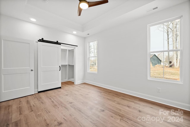 unfurnished bedroom featuring a barn door, light hardwood / wood-style floors, multiple windows, and ceiling fan