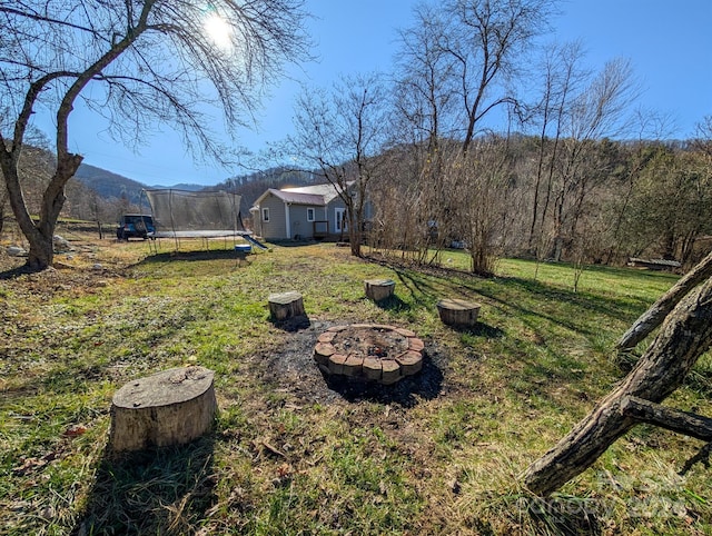 view of yard with a mountain view, a trampoline, and an outdoor fire pit