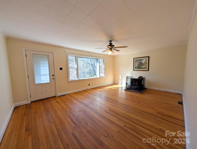 unfurnished living room with a wood stove, ceiling fan, hardwood / wood-style floors, and crown molding