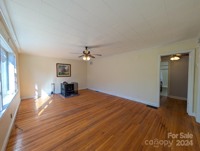 unfurnished living room with hardwood / wood-style floors, a wood stove, ceiling fan, and ornamental molding