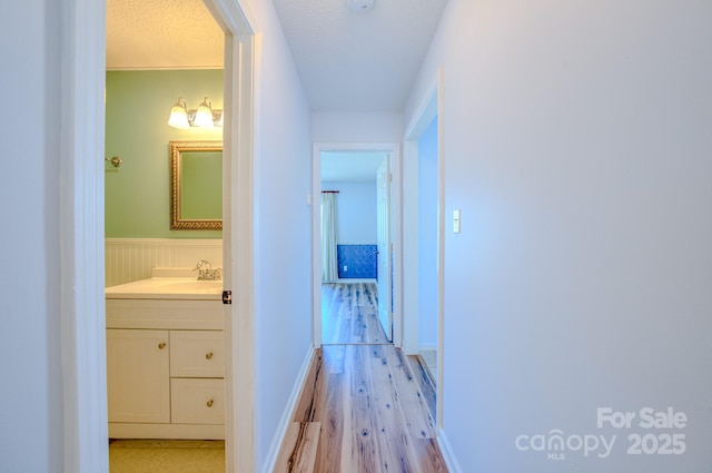 hallway featuring sink, a textured ceiling, and light wood-type flooring