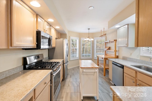 kitchen with stainless steel appliances, sink, light brown cabinets, a chandelier, and a kitchen island