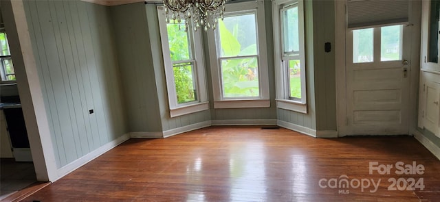 interior space with wood walls, an inviting chandelier, a wealth of natural light, and light hardwood / wood-style flooring