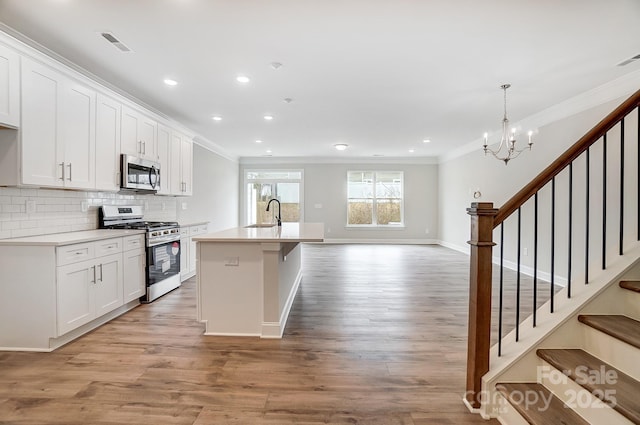 kitchen with decorative light fixtures, an island with sink, white cabinets, and stainless steel appliances