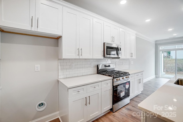 kitchen with white cabinets, appliances with stainless steel finishes, ornamental molding, and light wood-type flooring