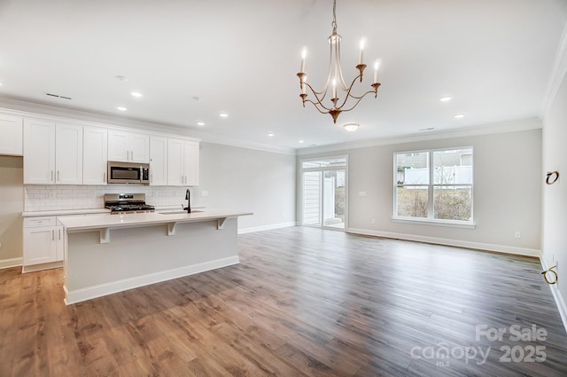 kitchen with appliances with stainless steel finishes, white cabinetry, a kitchen island with sink, sink, and decorative light fixtures