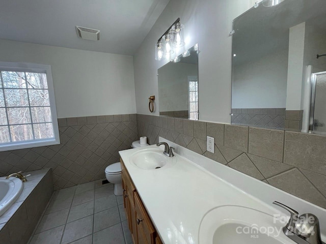 bathroom with a relaxing tiled tub, tile patterned floors, toilet, vanity, and tile walls