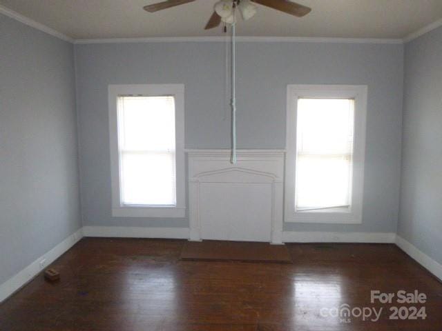 empty room with ornamental molding, plenty of natural light, and dark wood-type flooring