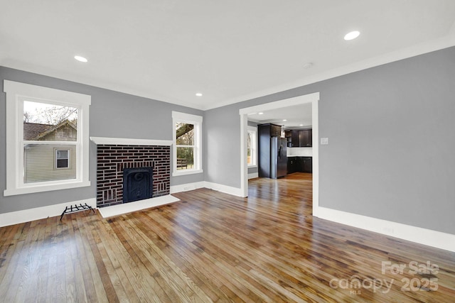 unfurnished living room featuring a brick fireplace, crown molding, and wood-type flooring