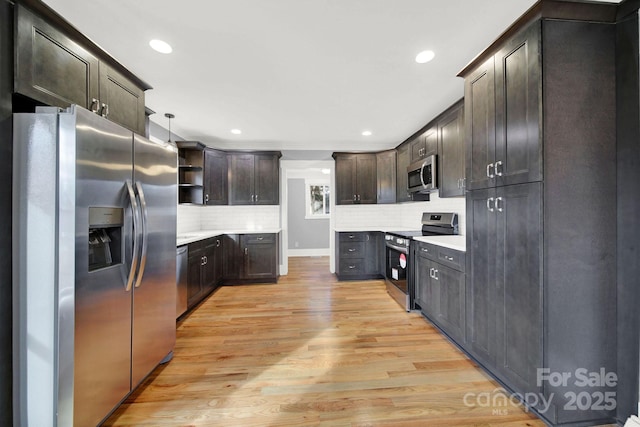 kitchen with appliances with stainless steel finishes, backsplash, hanging light fixtures, dark brown cabinetry, and light hardwood / wood-style floors