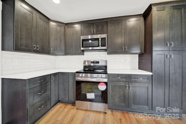 kitchen featuring stainless steel appliances, dark brown cabinets, light hardwood / wood-style floors, and decorative backsplash