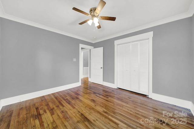 unfurnished bedroom featuring hardwood / wood-style flooring, crown molding, ceiling fan, and a closet