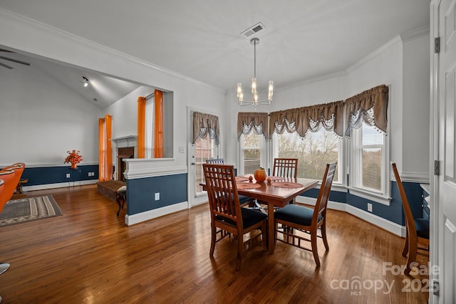 dining area with an inviting chandelier, lofted ceiling, ornamental molding, and dark hardwood / wood-style floors