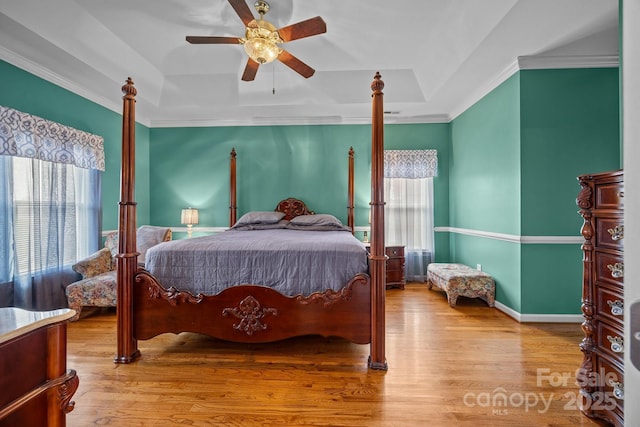 bedroom featuring crown molding, ceiling fan, light wood-type flooring, and a tray ceiling