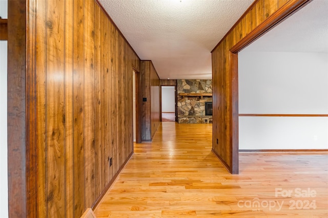 hall with wood walls, light hardwood / wood-style flooring, and a textured ceiling