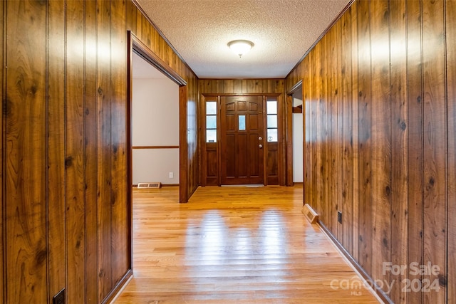 entryway with a textured ceiling, wooden walls, and light hardwood / wood-style flooring