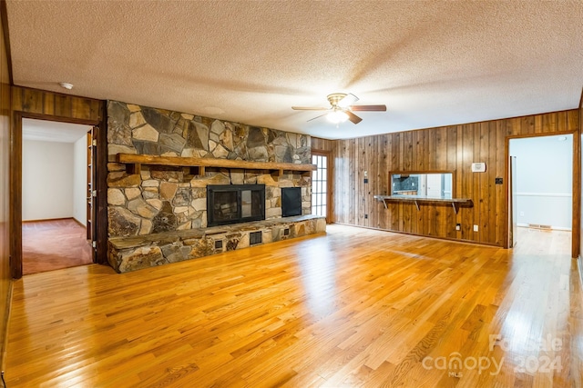 unfurnished living room featuring wood walls, hardwood / wood-style flooring, ceiling fan, a fireplace, and a textured ceiling