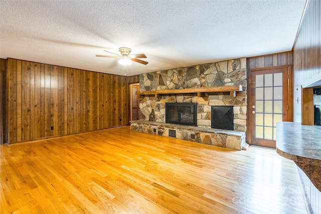 unfurnished living room featuring ceiling fan, wood-type flooring, a textured ceiling, wooden walls, and a fireplace