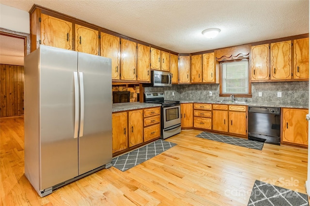 kitchen with sink, a textured ceiling, decorative backsplash, appliances with stainless steel finishes, and light wood-type flooring