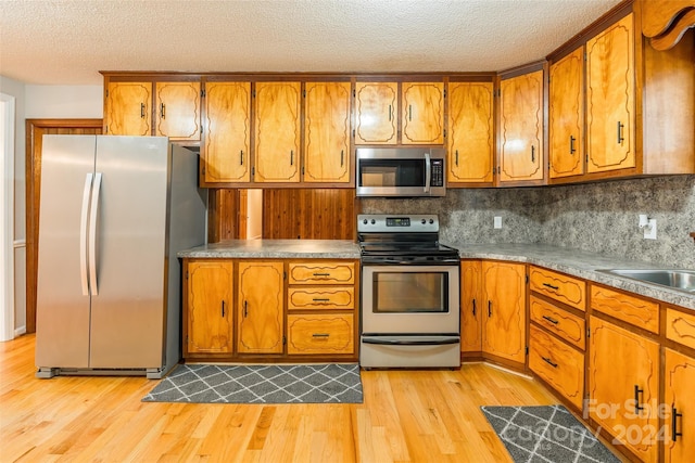 kitchen with sink, tasteful backsplash, light hardwood / wood-style floors, a textured ceiling, and appliances with stainless steel finishes