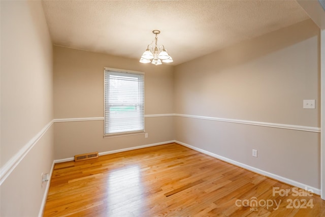 spare room with a textured ceiling, a notable chandelier, and hardwood / wood-style flooring