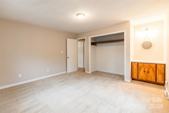 unfurnished bedroom featuring a textured ceiling, light colored carpet, and a closet