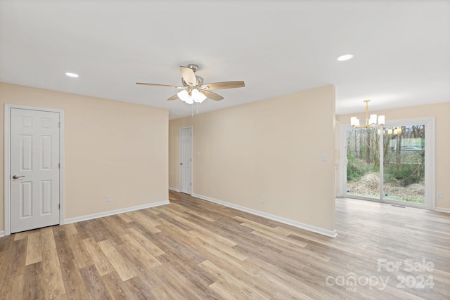 empty room featuring ceiling fan with notable chandelier and light wood-type flooring