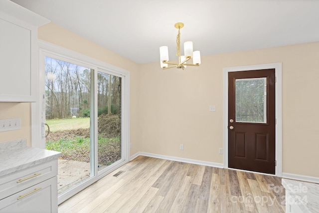 unfurnished dining area featuring light hardwood / wood-style flooring, a healthy amount of sunlight, and an inviting chandelier