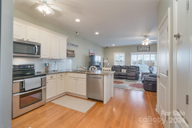 kitchen with kitchen peninsula, white cabinetry, light hardwood / wood-style floors, and appliances with stainless steel finishes