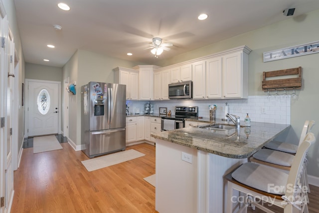 kitchen with kitchen peninsula, appliances with stainless steel finishes, sink, light hardwood / wood-style flooring, and white cabinets