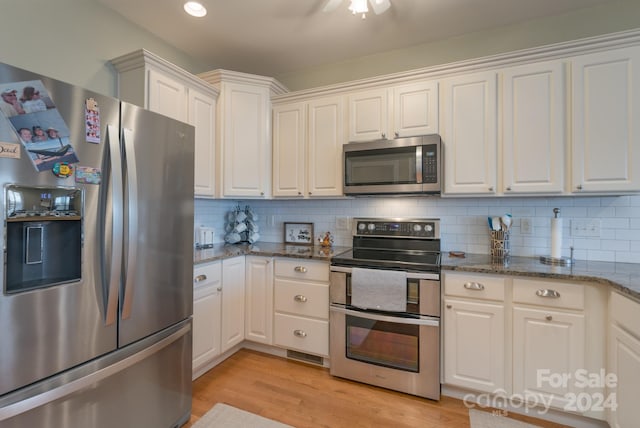 kitchen featuring white cabinetry, stainless steel appliances, tasteful backsplash, light hardwood / wood-style flooring, and dark stone countertops