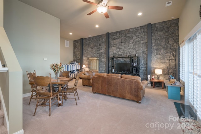 living room featuring light colored carpet, a wood stove, and ceiling fan