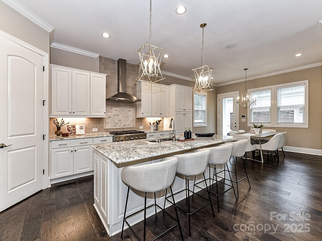 kitchen featuring sink, wall chimney range hood, white cabinets, an island with sink, and range